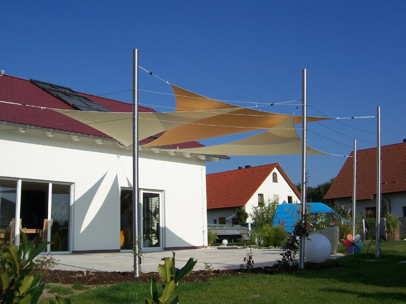 Sonnensegel aus Netzgewebe an Edelstahlmasten über der Terrasse eines Wohnhauses