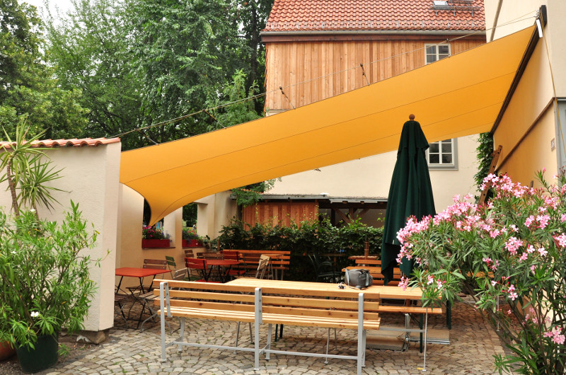 Gelbes wandelbares Dach über einer Terrasse mit Biertischen